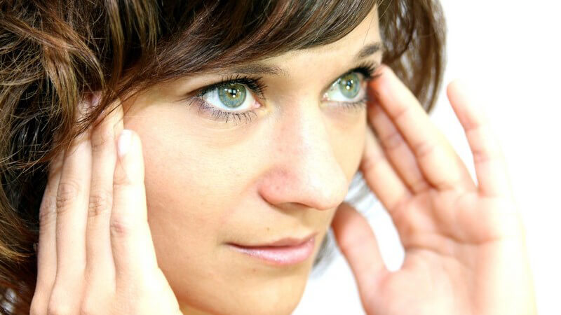 Dunkelhaarige Frau mit Kopfschmerzen fasst sich an die Schläfen