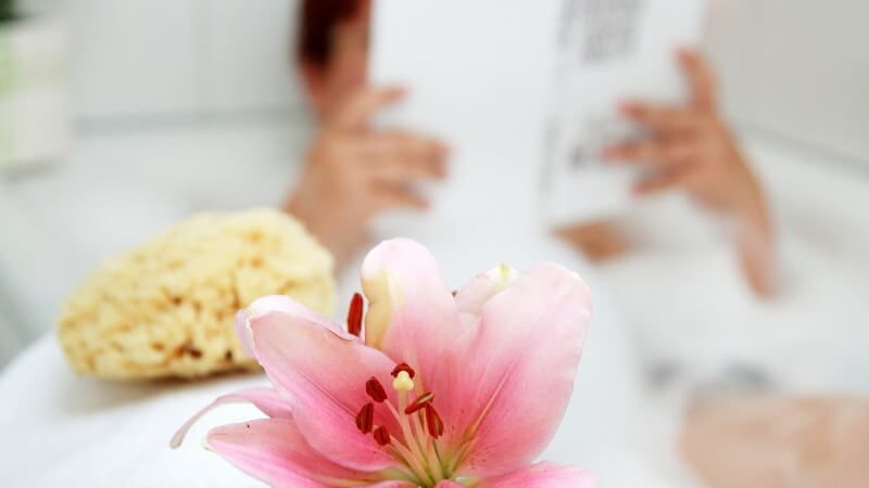 Frau in Badewanne nimmt Schaumbad und liest ein Buch