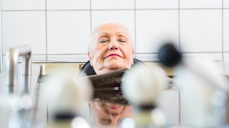 Seniorin liegt entspannt in einer Stahlwanne und nimmt ein Moorbad