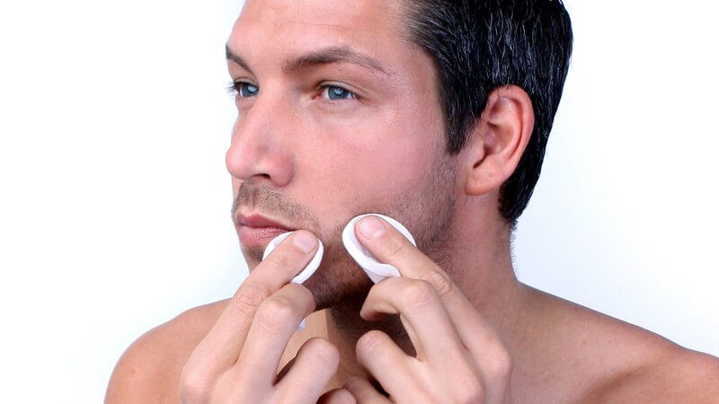 Junger Mann drückt Pickel mit Wattepads aus, weißer Hintergrund