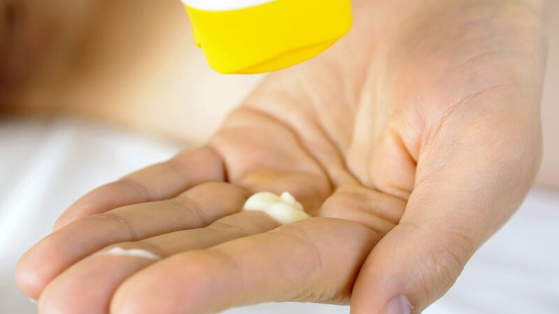 Frau quetscht Salbe oder Creme aus einer weiß-gelben Flasche in die Hand