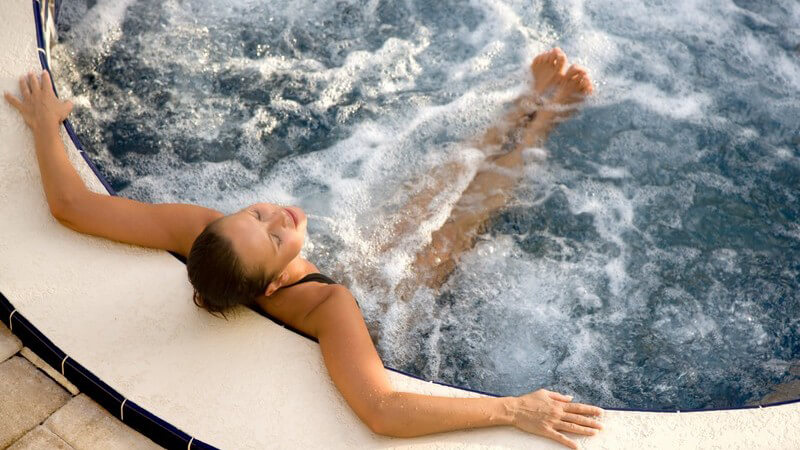 Ansicht von oben: Junge Frau relaxt im Outdoor-Whirlpool