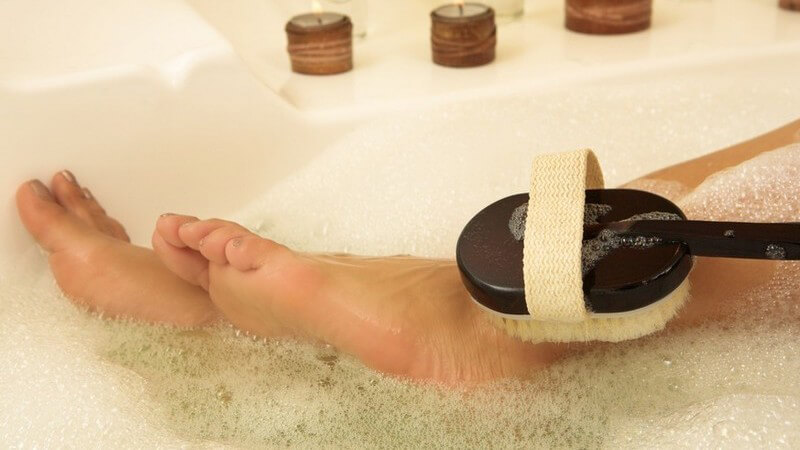 Frauenfüße in Badewanne mit Schaum und Kerzen, die von Massagebürste gereinigt werden