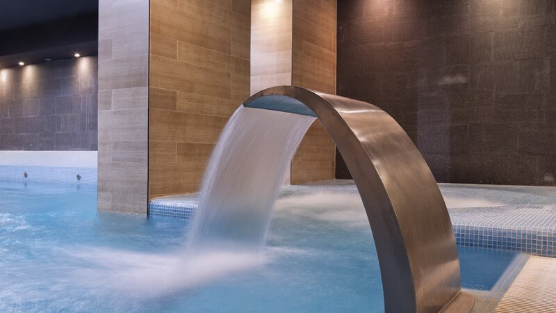 Bronzefarbene Wasserfall-Jetdusche in einer Poollandschaft im Spa