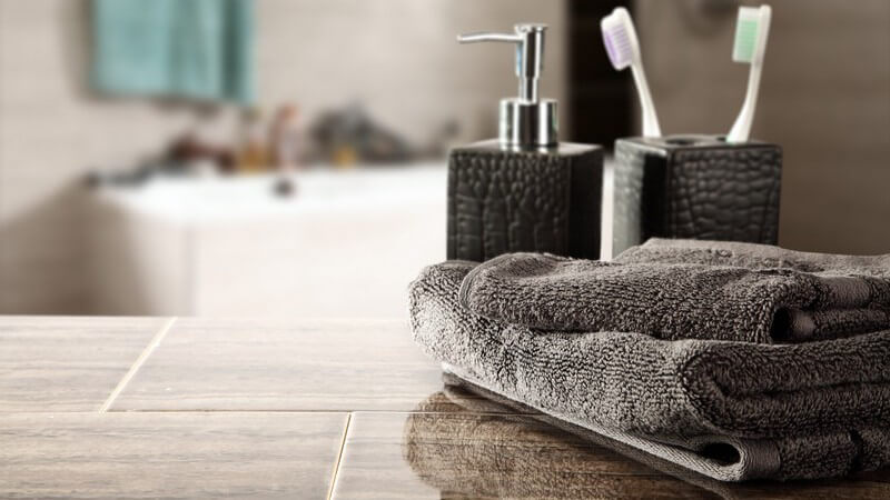 Modernes Badezimmer mit grauem Seifenspender, Zahnputzbecher und Handtüchern im Vordergrund