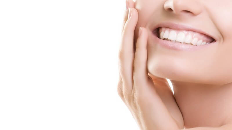 Untere Gesichtshälfte einer jungen Frau, lächelnd mit weißen Zähnen, rechte Hand an der Wange, vor weißem Hintergru