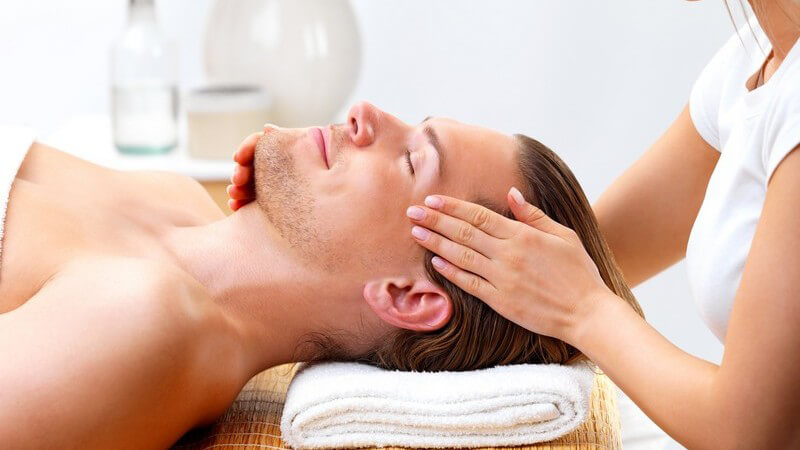 Mann liegt auf dem Rücken, lässt sich das Gesicht von blonder Frau massieren