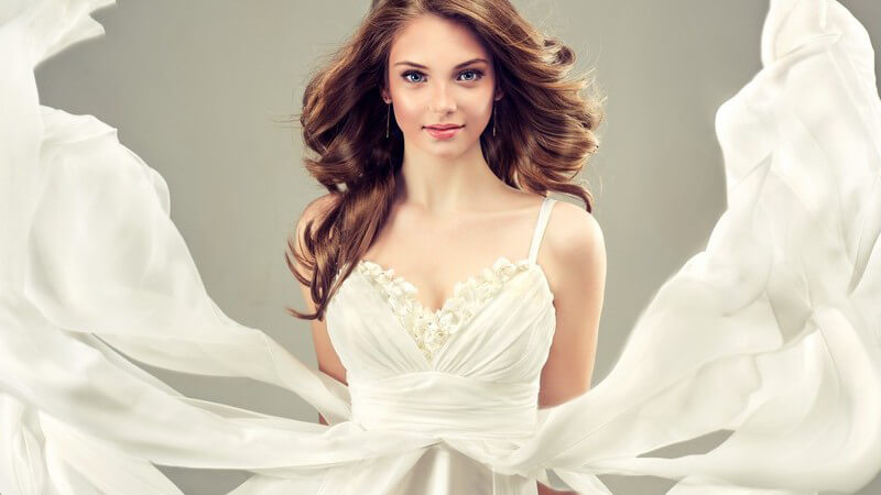 Junges Model in weißem Brautkleid vor grauem Hintergrund, der Stoff weht nach oben