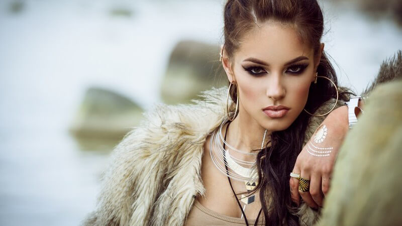 Model mit langen braunen Haaren und Pelzmantel, trägt jede Menge Schmuck und eine Bemalung auf dem Handrücken