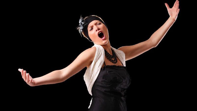 Opernsängerin mit schwarzem Kleid und Stirnband singt vor einem schwarzen Hintergrund