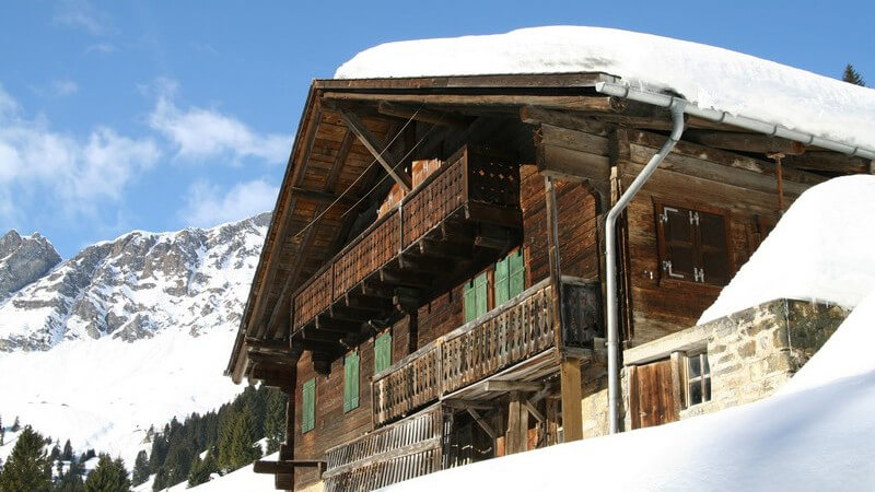 Holzhütte in Winterlandschaft, im Hintergrund Berge