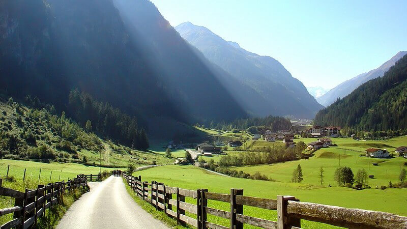 Berglandschaft, Weg zwischen grünen Wiesen und Bergen, strahlend blauer Himmel