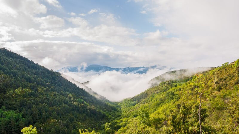Blick über grüne Berge und Täler, in der Ferne eine große Wolkenfront