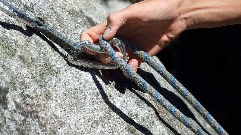 Hand an Karabinerhaken an Fels, Klettern