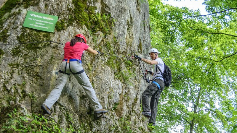Paar mit Helm beim Klettern an einem Kletterfelsen im Oberlandsteig