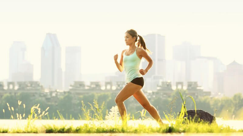 Im Sonnenlicht laufende Frau mit Skyline im Hintergrund