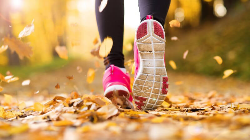 Joggen im Herbst - Laufschuhe auf Waldweg mit Herbstlaub