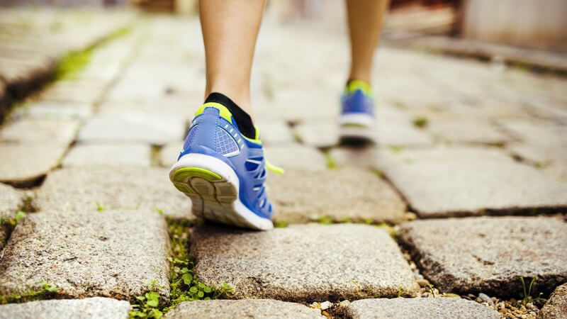 Frauenbeine mit blauen Laufschuhen auf Kopfsteinpflaster