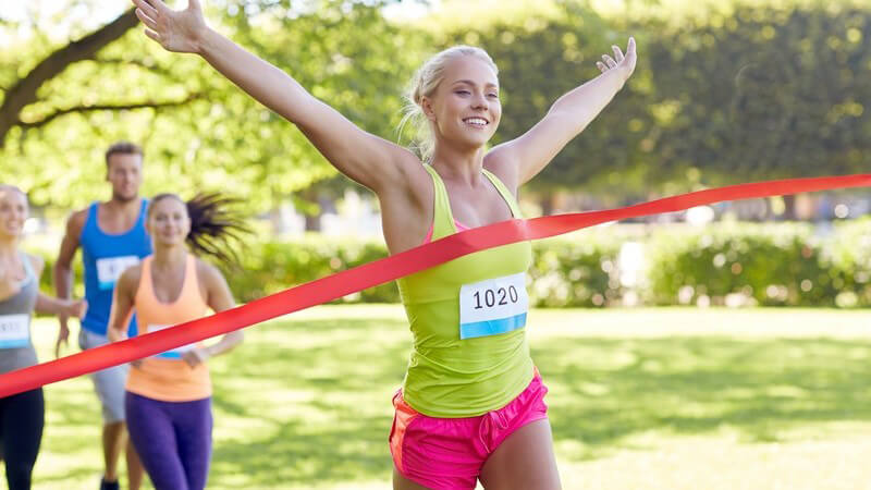 Blonde Läuferin erreicht jubelnd das rote Zielband