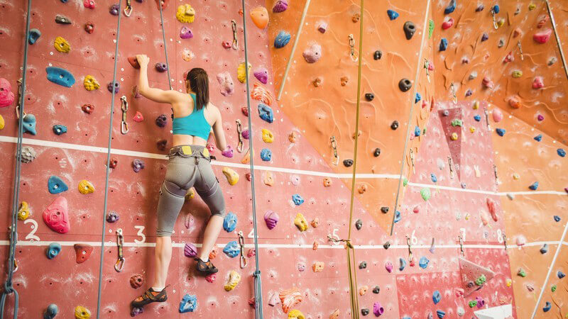 Frau beim Bouldern, alleine an einer riesigen Kletterwand