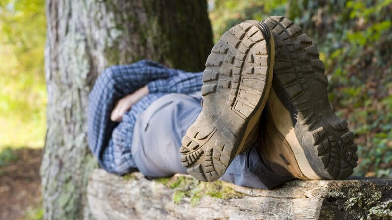 Wanderer liegt auf Holzbank im Wald