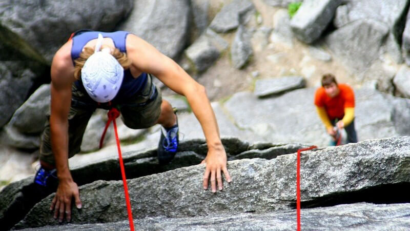 Bergsteigen bei Felsen und Granit-Klippen, oben Bergsteiger mit weißem Helm, unten sichert ein Zweiter mit Seil