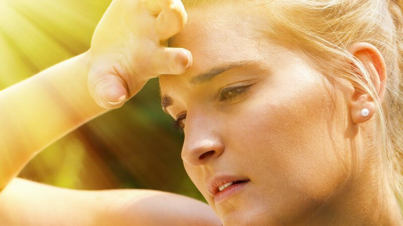 Junge Frau im heißen Sonnenlicht fasst sich erschöpft an die Stirn