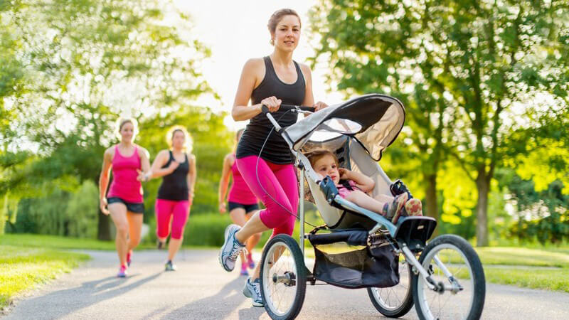 Joggerin mit Kind im Sport-Kinderwagen läuft durch den Park
