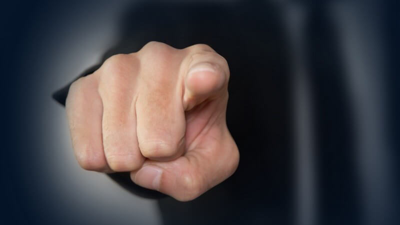 Nahaufnahme einer mahnenden Hand von vorne, geballte Faust mit ausgestrecktem Zeigefinger vor dunklem Hintergrund