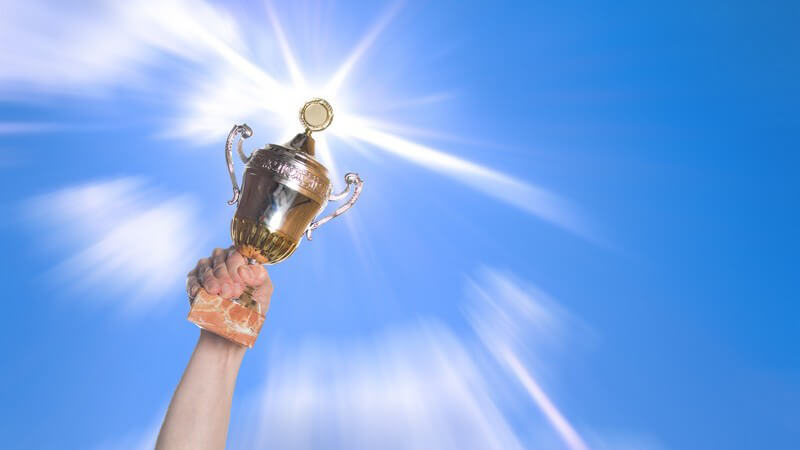 Hand hält Pokal nach oben unter blauem Himmel