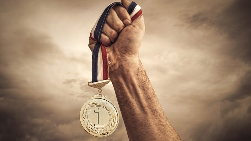 Zum Himmel gestreckter Arm mit Sieger-Medaille in der Hand