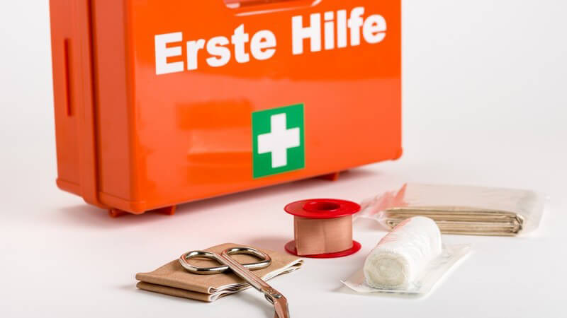 Verbandsmaterial wie Pflaster, Schere und Mullbinde liegen vor einem Erste Hilfe-Verbandskasten