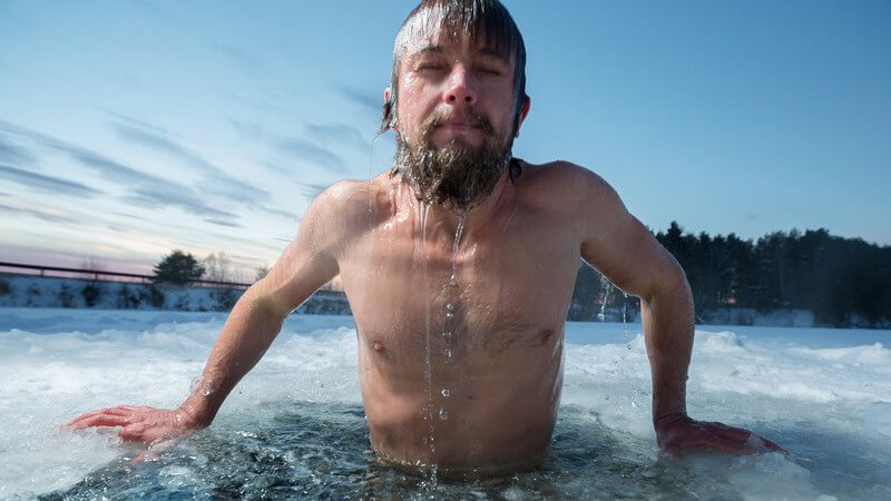 Mann mit Vollbart badet in einem Loch in der Eisdecke eines zugefrorenen Sees