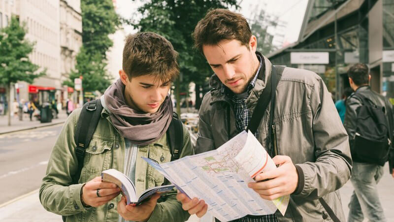 Zwei junge Männer stehen in einer Straße und gucken auf einen Stadtplan