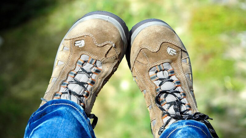 Wanderschuhe aus hellem Leder, ein Teil der Beine, im Hintergrund Wiese