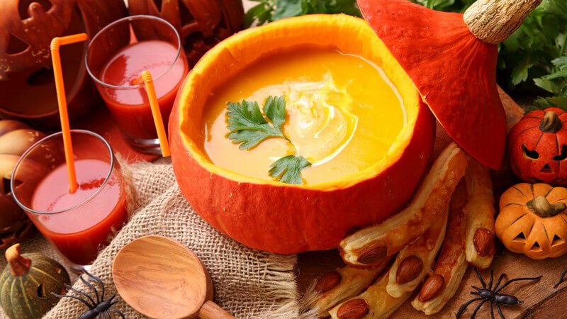 Kürbissuppe in aufgeschnittenem Kürbis, daneben Halloween-Dekoration