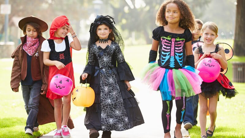 Kinder in Halloween-Kostümen spazieren mit Kürbis-Laternen einen Gehweg entlang