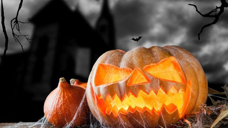 Halloween - Kürbisfratze leuchtet, im Hintergrund Burg, schwarze Wolken, Fledermaus