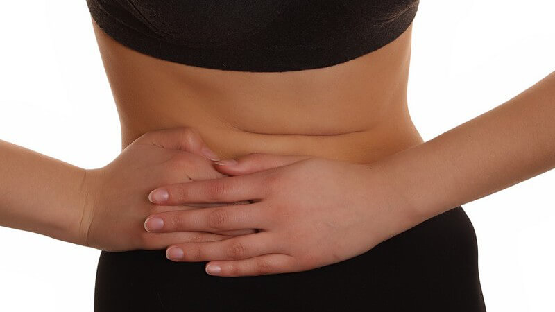Frau hält sich vor Schmerzen Hände auf nackten Bauch