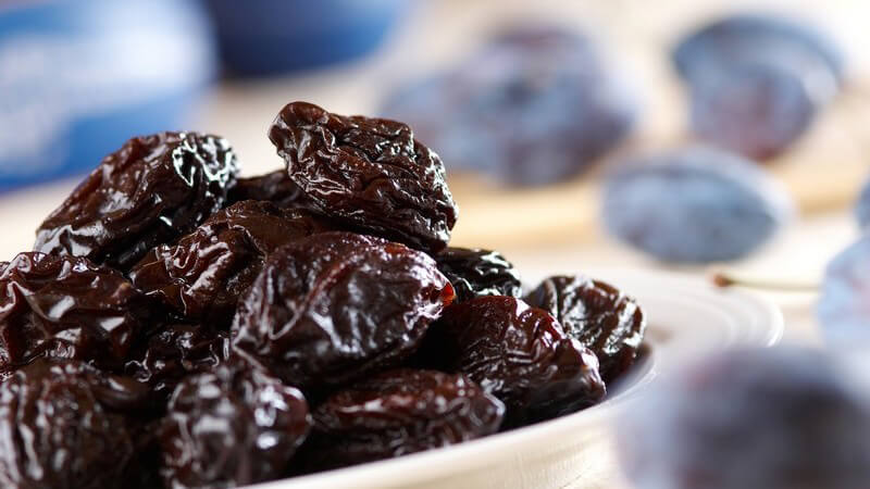 Getrocknete Pflaumen auf Teller, im Hintergrund frische Pflaumen