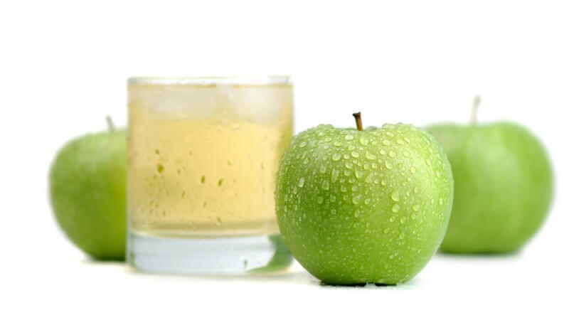 Glas mit Apfelsaft und Eiswürfeln, daneben frische grüne Äpfel