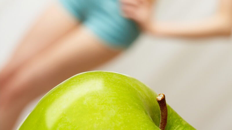 Grüner Apfel, im Hintergrund Frau in kurzer Shorts