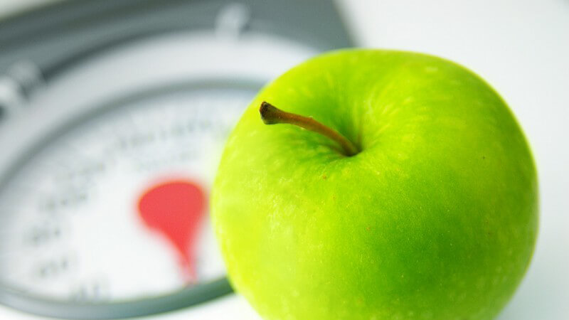 Grüner Apfel auf einer analogen Körperwaage mit rotem Zeiger