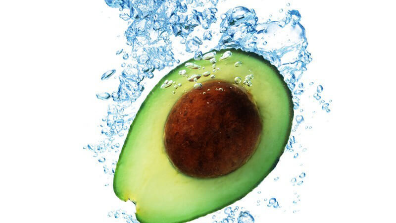 Aufgeschnittene Avocado fällt ins Wasser und hinterlässt Wasserblasen unter Oberfläche