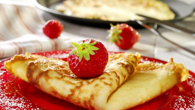 Frischer Pfannkuchen mit Erdbeeren auf Teller, im Hintergrund Pfanne