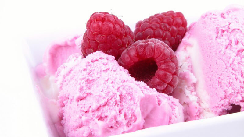 Rosa Fruchteis, darauf drei frische Himbeeren