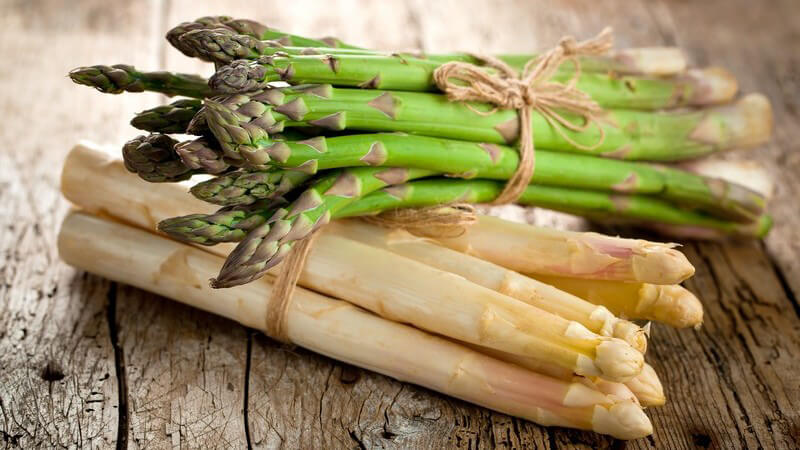 Je ein Bündel weißer und grüner Spargel liegen auf einem Holztisch
